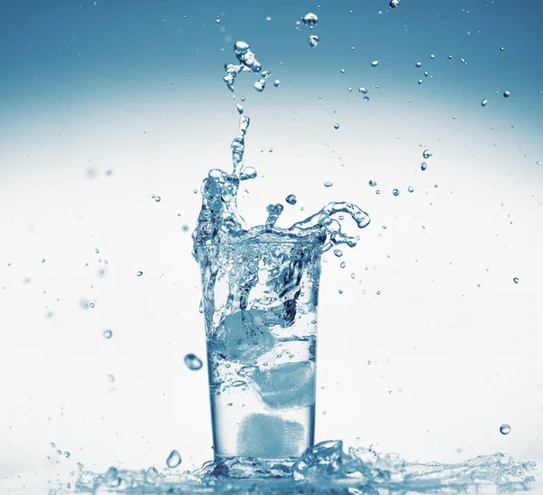 Один стакан воды с брызгами от падающего кубика льда, белый фон, изолированный объект — стоковое фото