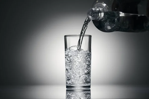 Sprudelndes Wasser in ein Glas auf dunklem Hintergrund gießen — Stockfoto