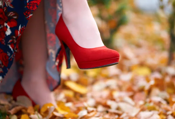Close up of women's feet shod in red high heels shoes, autumn season, yellow fallen leaves as background — Stock Photo, Image