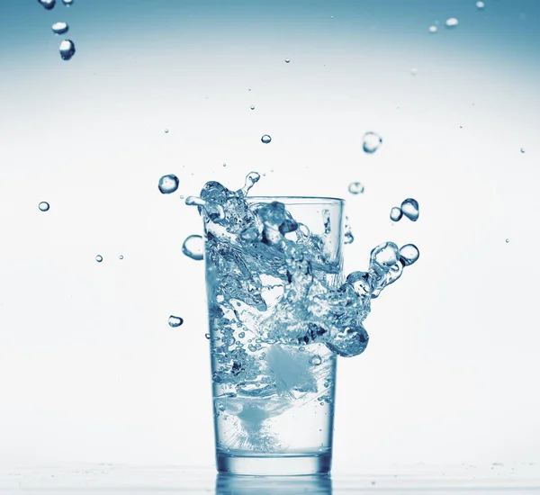 Un pahar de apă cu stropire din cubul de gheață care cade, fundal alb, obiect izolat — Fotografie, imagine de stoc