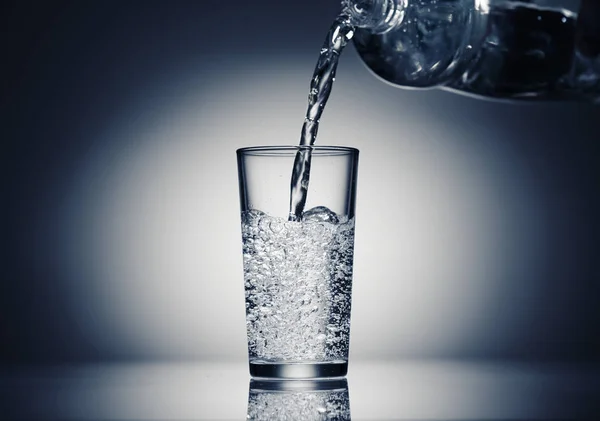 Nalewanie wody gazowanej do szklanki na ciemnoniebieskim tle — Zdjęcie stockowe