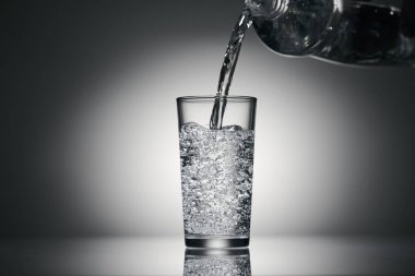 Karanlık bir arka planda bardağa köpüklü su dökmek