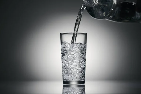 Derramando água espumante em um copo em um fundo escuro — Fotografia de Stock