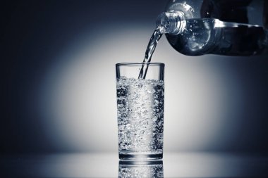 Koyu mavi arka planda bir bardağa köpüklü su dökerek