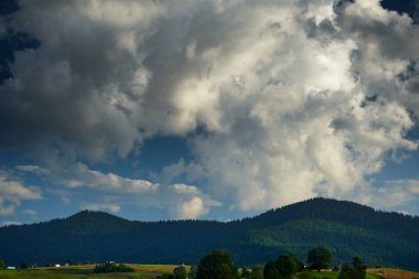 Karpat dağlarında gün batımı - güzel yaz manzarası, tepelerde yaylalar, karanlık bulutlu gökyüzü ve parlak güneş ışığı, çayır ve kır çiçekleri