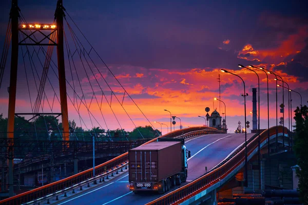 橋の上をコンテナで走るトラック、美しい夕日、工業港の貨物車、道路が上がる — ストック写真