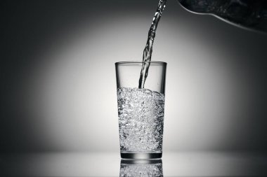 Karanlık bir arka planda bardağa köpüklü su dökmek