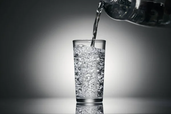 Wlewanie wody gazowanej do szklanki na ciemnym tle — Zdjęcie stockowe