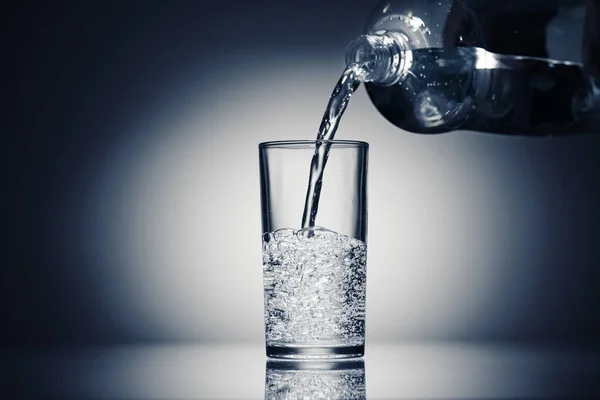 Nalewanie wody gazowanej do szklanki na ciemnoniebieskim tle — Zdjęcie stockowe