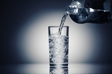 Koyu mavi arka planda bir bardağa köpüklü su dökerek