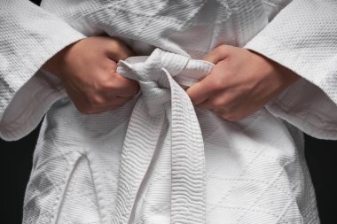 Dövüş sanatları kıyafeti giymiş genç bir sporcunun elleri, koyu gri bir arka planda, bir spor konseptinde poz verir.