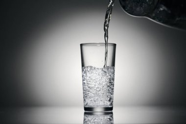 Karanlık bir arka planda bardağa köpüklü su dökmek