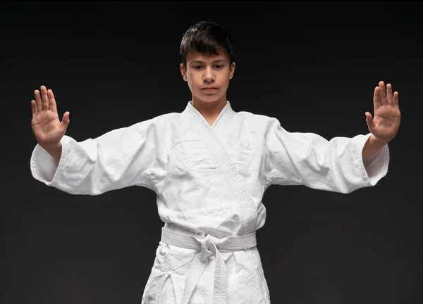 Portrait of a teenager dressed in martial arts clothing poses on a dark gray background, a sports concept — Stock Photo, Image