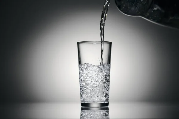 Verter agua con gas en un vaso sobre un fondo oscuro — Foto de Stock