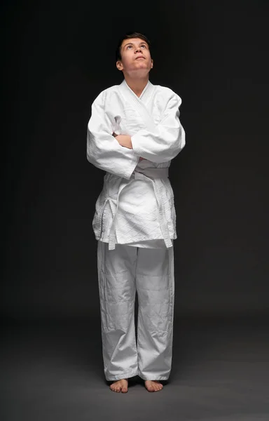 En tonåring klädd i kampsport kläder poser på en mörkgrå bakgrund, en sport koncept — Stockfoto