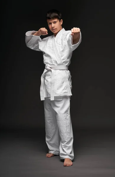 A teenager dressed in martial arts clothing poses on a dark gray background, a sports concept — Stock Photo, Image