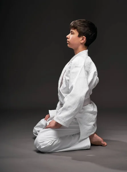 Concepto de deporte - un adolescente vestido con ropa de artes marciales posa sobre un fondo gris oscuro, sesión de estudio —  Fotos de Stock