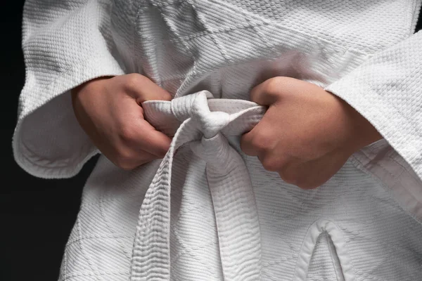 Mani da vicino di un atleta adolescente, vestito con abiti di arti marziali posa su uno sfondo grigio scuro, un concetto sportivo — Foto Stock