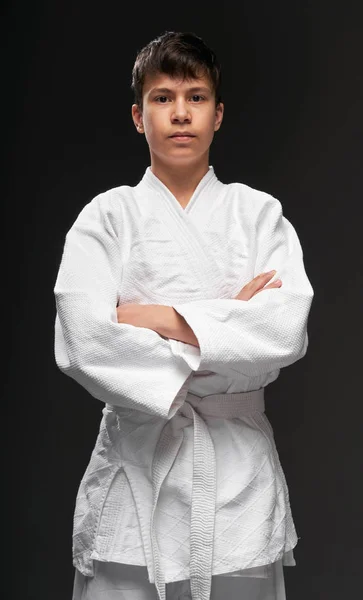 Portrét teenagera oblečeného v bojových uměleckých oděvech pózuje na tmavě šedém pozadí, sportovní koncept — Stock fotografie
