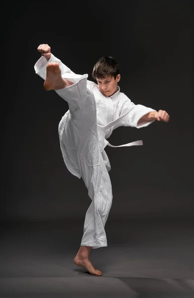 Een tiener gekleed in vechtsport kleding poseert op een donkergrijze achtergrond, een sport concept — Stockfoto