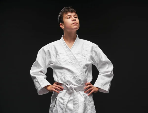 Sport concept - a proud teenager dressed in martial arts clothing poses on a dark gray background, studio shoot — 스톡 사진