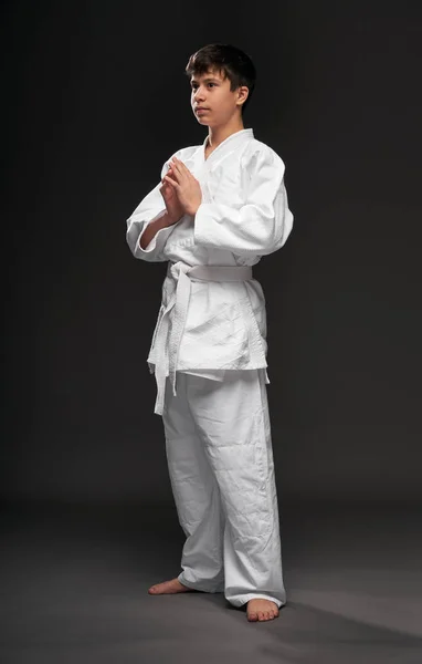 Teenager oblečený do bojových umění oblečení pózuje na tmavě šedém pozadí, sportovní koncept — Stock fotografie