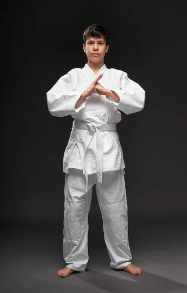 Un adolescente vestido con ropa de artes marciales posa sobre un fondo gris oscuro, un concepto deportivo —  Fotos de Stock