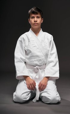 Spor konsepti - Dövüş sanatları kıyafeti giymiş bir genç koyu gri arka planda poz verir, stüdyo çekimi