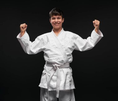 Spor konsepti - Dövüş sanatları kıyafeti giymiş bir genç koyu gri arka planda poz verir, stüdyo çekimi