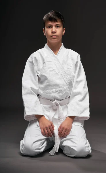 Concepto de deporte - un adolescente vestido con ropa de artes marciales posa sobre un fondo gris oscuro, sesión de estudio — Foto de Stock