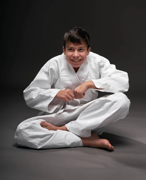 Concepto de deporte - un adolescente vestido con ropa de artes marciales posa sobre un fondo gris oscuro, sesión de estudio —  Fotos de Stock