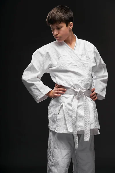 Sport koncept - teenager oblečený v bojových umění oblečení pózuje na tmavě šedém pozadí, studio střílet — Stock fotografie