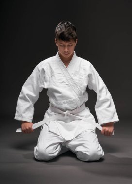 Spor konsepti - Dövüş sanatları kıyafeti giymiş bir genç koyu gri arka planda poz verir, stüdyo çekimi