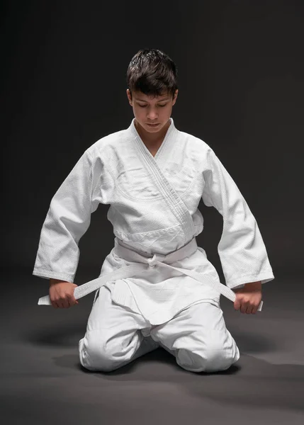 Concept de sport - un adolescent habillé en vêtements d'arts martiaux pose sur un fond gris foncé, tournage en studio — Photo