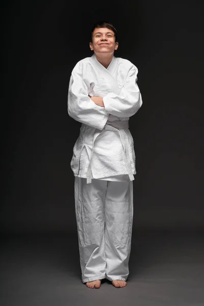 Uma adolescente vestida com roupas de artes marciais posa e se divertindo em um fundo cinza escuro, um conceito esportivo — Fotografia de Stock