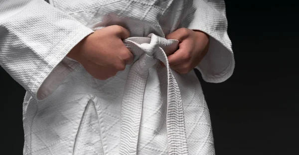 Hands close up of a teenager athlete, dressed in martial arts clothing poses on a dark gray background, a sports concept — Stock Photo, Image