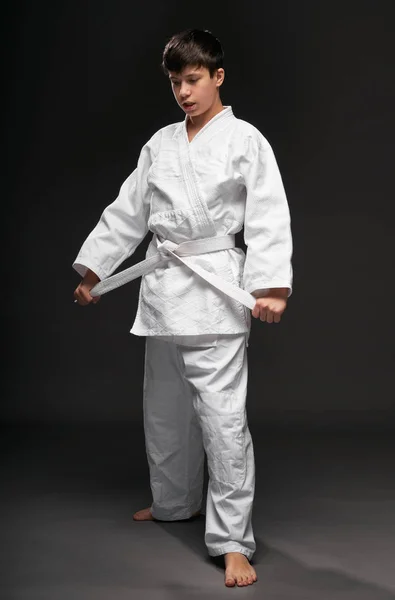 Concepto de deporte - un adolescente vestido con ropa de artes marciales posa sobre un fondo gris oscuro, sesión de estudio — Foto de Stock