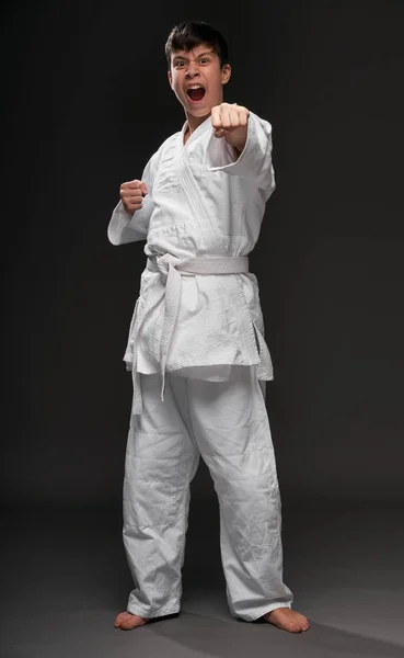 Un adolescente vestido con ropa de artes marciales posando y llorando sobre un fondo gris oscuro, un concepto deportivo — Foto de Stock