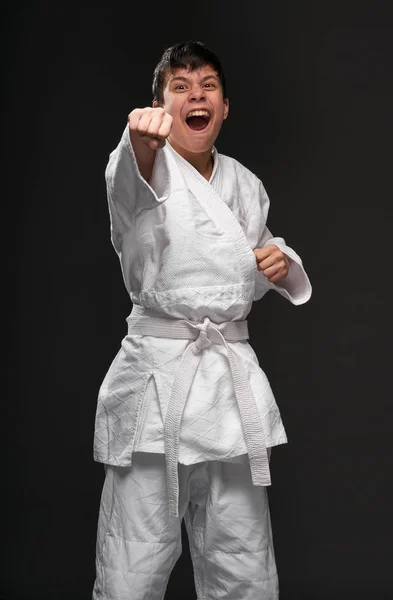 A teenager dressed in martial arts clothing posing and crying on a dark gray background, a sports concept — Stock Photo, Image