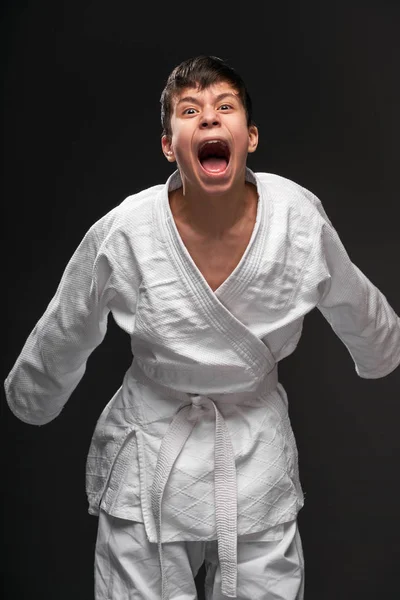 Un adolescente vestido con ropa de artes marciales posando y llorando sobre un fondo gris oscuro, un concepto deportivo —  Fotos de Stock