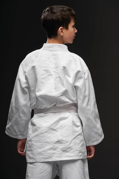 武道の服を着た10代の若者の裏側の景色は、暗い灰色の背景、スポーツの概念にポーズ — ストック写真