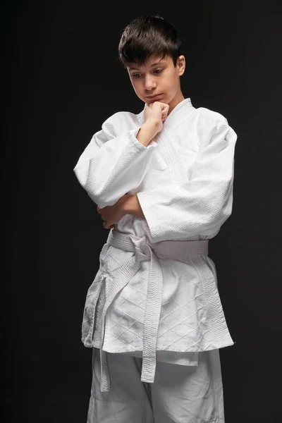 Een tiener gekleed in vechtsport kleding poseert op een donkergrijze achtergrond, een sport concept — Stockfoto