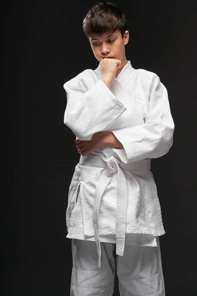 Sport concept - een tiener gekleed in vechtsport kleding poseert op een donkergrijze achtergrond, studio shoot — Stockfoto