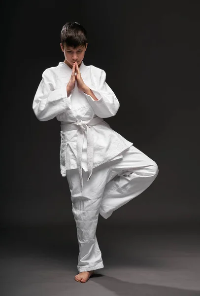 Un adolescente vestido con ropa de artes marciales posa sobre un fondo gris oscuro, un concepto deportivo —  Fotos de Stock