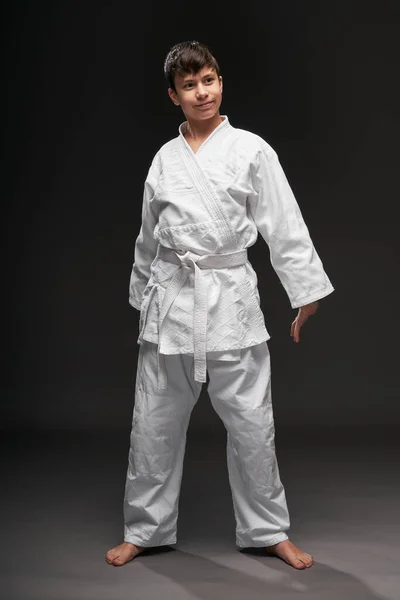 मार्शल आर्ट्स वस्त्रों में पहने हुए एक किशोर एक अंधेरे ग्रे पृष्ठभूमि पर खड़ा है, एक खेल अवधारणा — स्टॉक फ़ोटो, इमेज