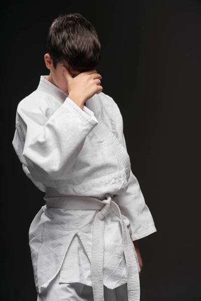 Un adolescente triste vestido con ropa de artes marciales que tiene problemas sobre un fondo gris oscuro, un concepto deportivo — Foto de Stock