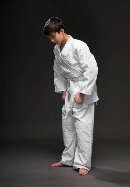 Nastolatek ubrany w odzież sztuk walki stanowi na ciemnym szarym tle, koncepcja sportowa — Zdjęcie stockowe