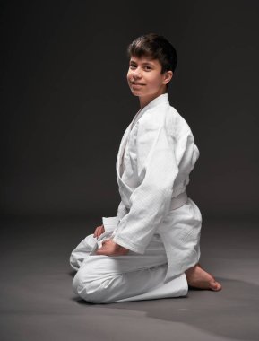 Spor konsepti - Dövüş sanatları kıyafeti giymiş bir genç koyu gri arka planda poz verir, stüdyo çekimi