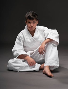 Spor konsepti - Dövüş sanatları kıyafeti giymiş bir genç koyu gri arka planda poz verir, stüdyo çekimi