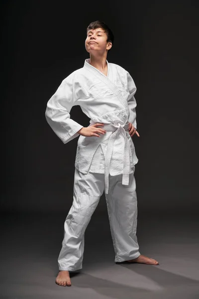 Un adolescente vestido con ropa de artes marciales posa sobre un fondo gris oscuro, un concepto deportivo —  Fotos de Stock